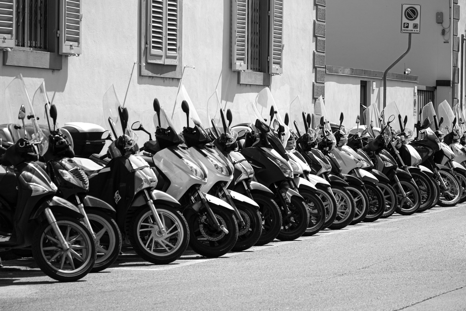 A row of parked motorcycles in black and white along a street, highlighting urban transportation.