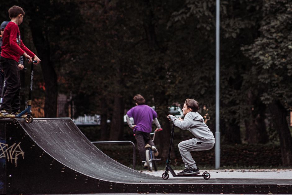 Kids having fun riding scooters on a ramp at an outdoor skate park.